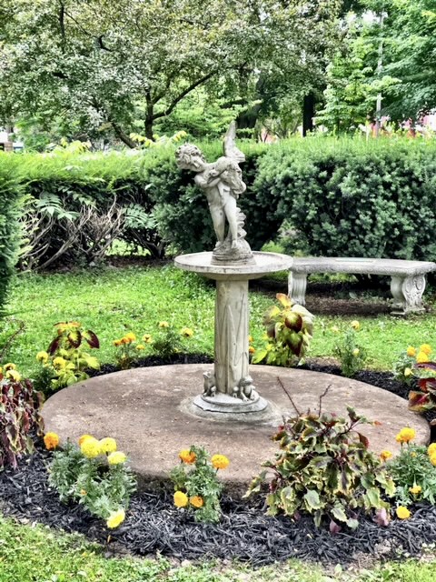 Borland bird font with flowers around the base and a stone bench and hedge behind it